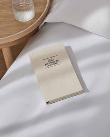 The Five Minute Journal on white bedding beside a wooden table.