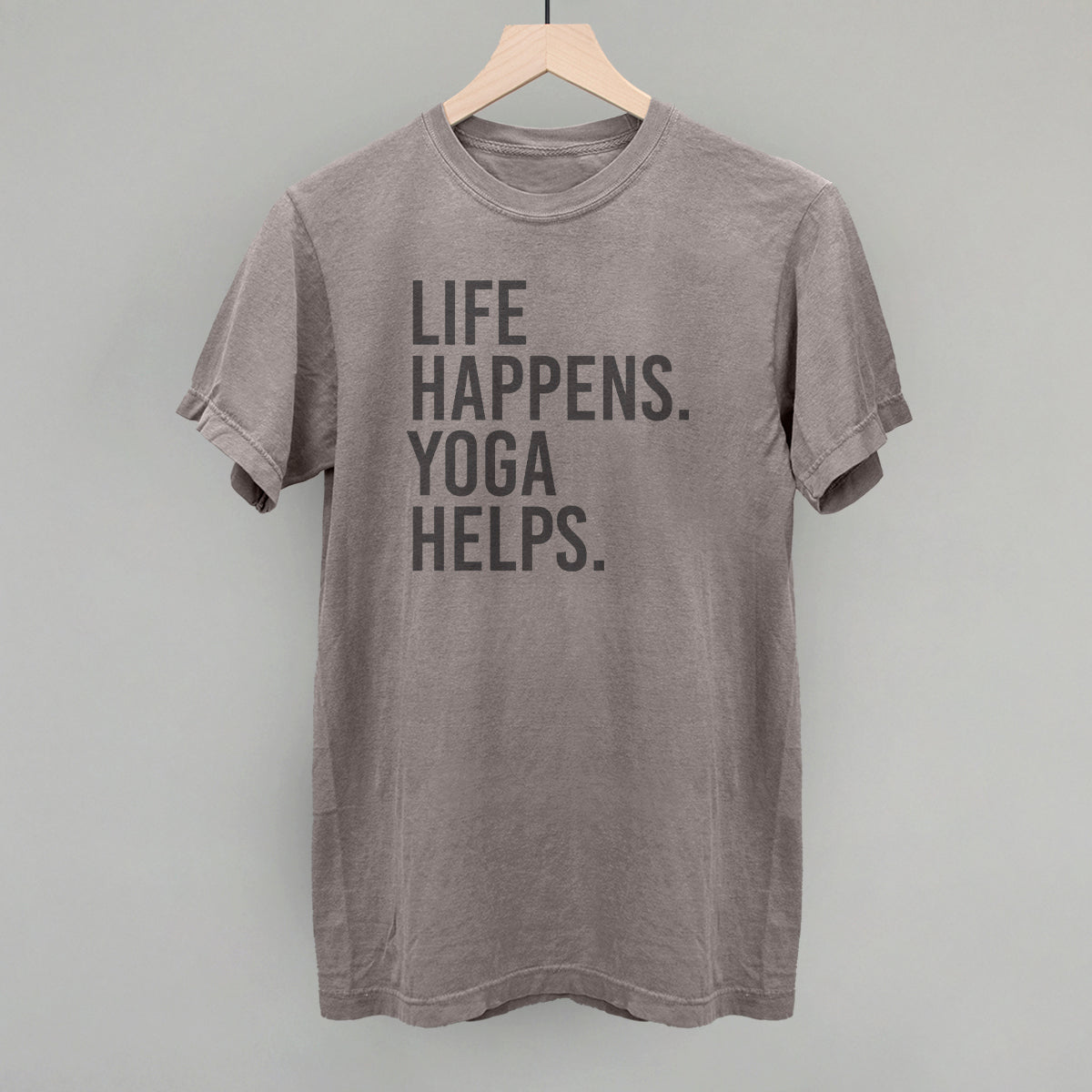 Taupe short-sleeve shirt on a hanger with visible printed text, Life Happens. Yoga Helps.