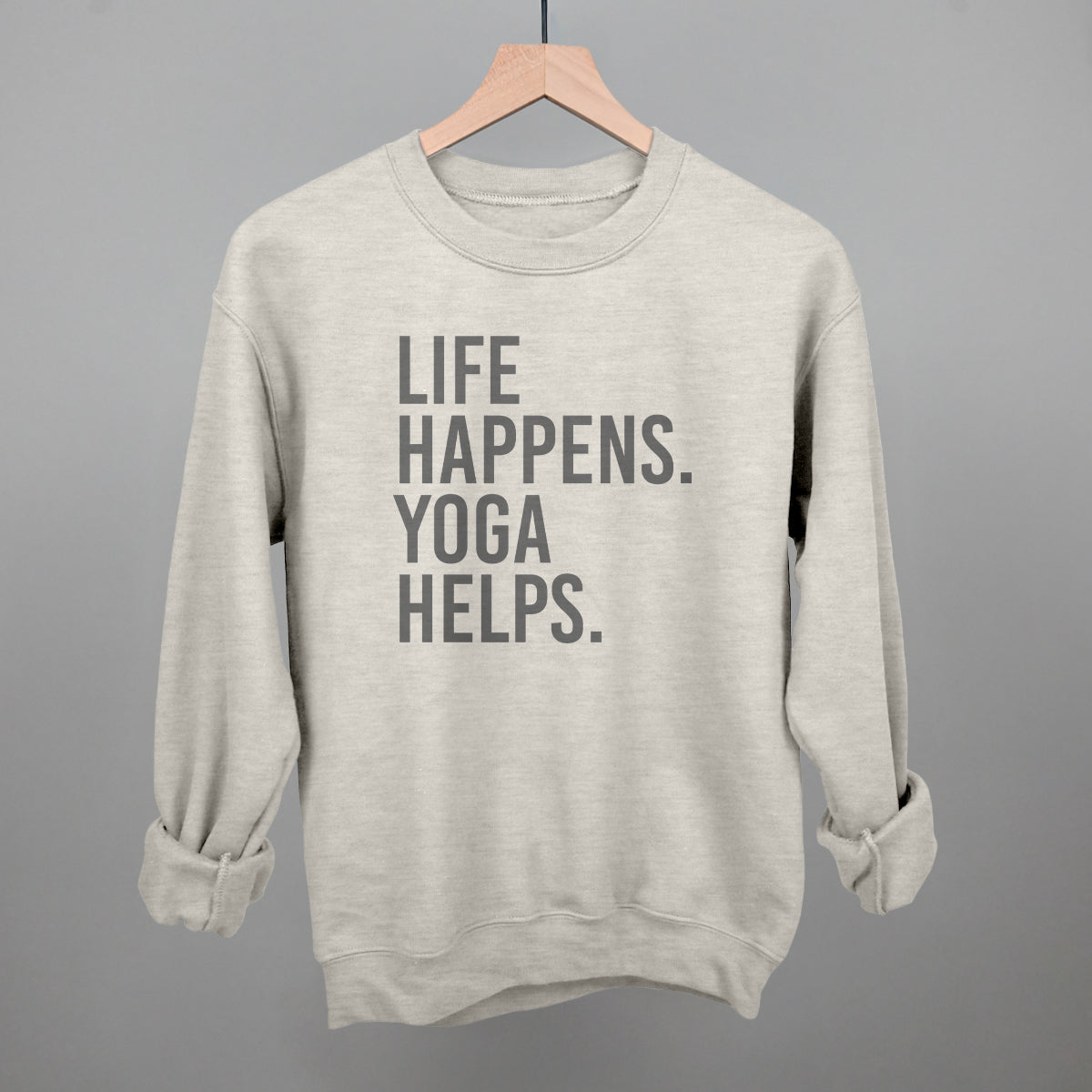 Light gray sweatshirt on a hanger with visible printed text, Life Happens. Yoga Helps.