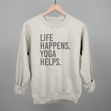 Light gray sweatshirt on a hanger with visible printed text, Life Happens. Yoga Helps.