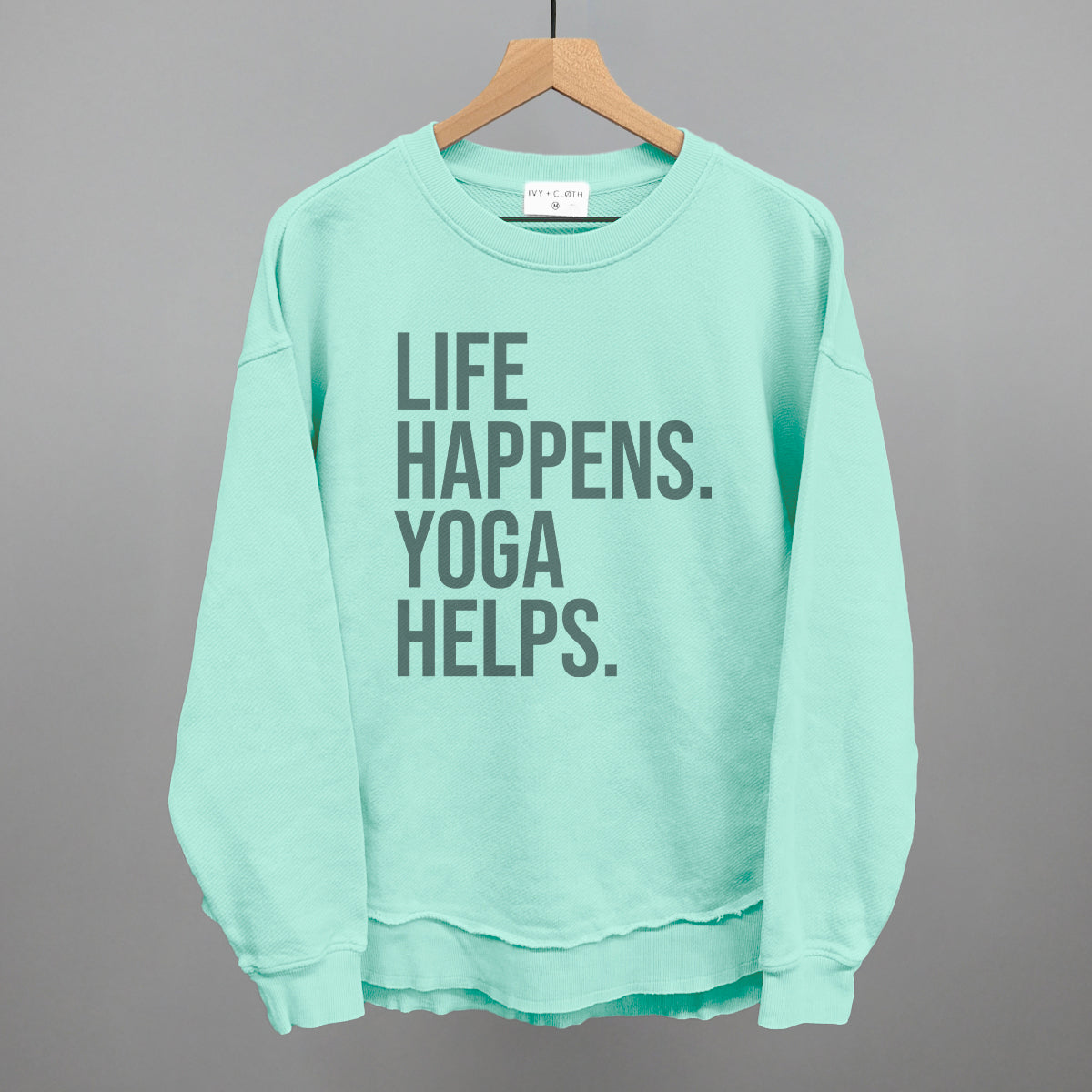 Mint textured long-sleeve top on a hanger with visible printed text, Life Happens. Yoga Helps.
