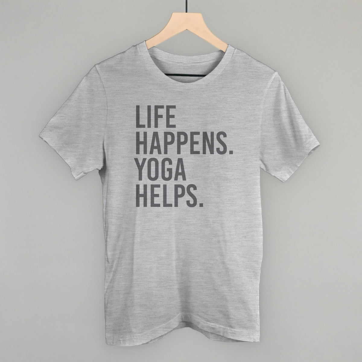 Light gray short-sleeve shirt on a hanger with visible printed text, Life Happens. Yoga Helps.