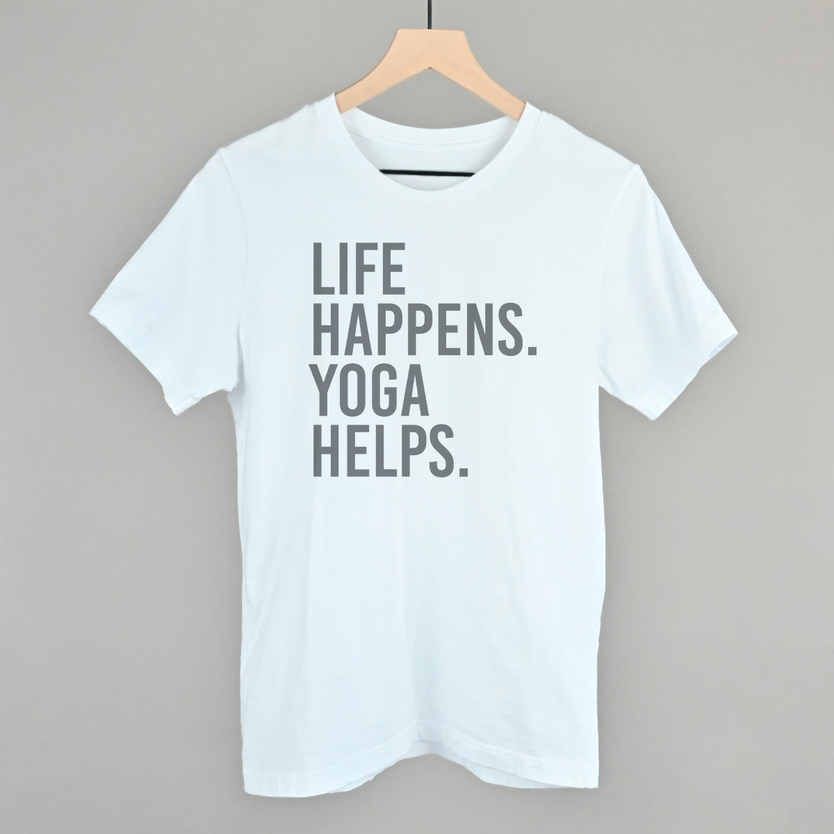 White short-sleeve shirt on a hanger with visible printed text, Life Happens. Yoga Helps.