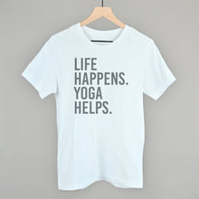 White short-sleeve shirt on a hanger with visible printed text, Life Happens. Yoga Helps.