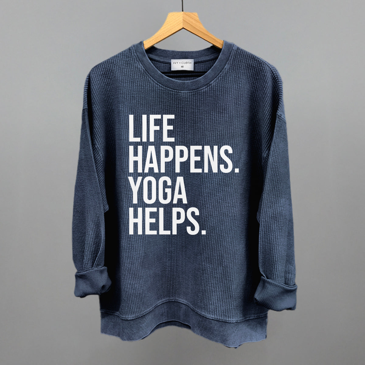Dark blue textured long-sleeve top on a hanger with visible printed text, Life Happens. Yoga Helps.
