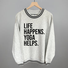 Light gray striped-trim sweatshirt on a hanger with visible printed text, Life Happens. Yoga Helps.