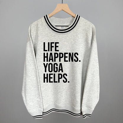 Light gray striped-trim sweatshirt on a hanger with visible printed text, Life Happens. Yoga Helps.
