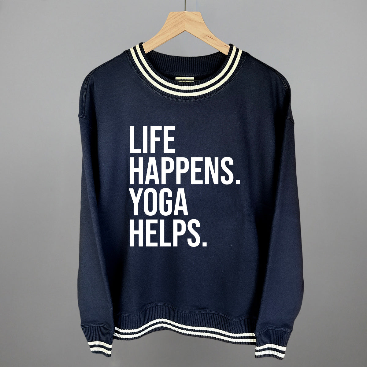 Navy striped-trim sweatshirt on a hanger with visible printed text, Life Happens. Yoga Helps.
