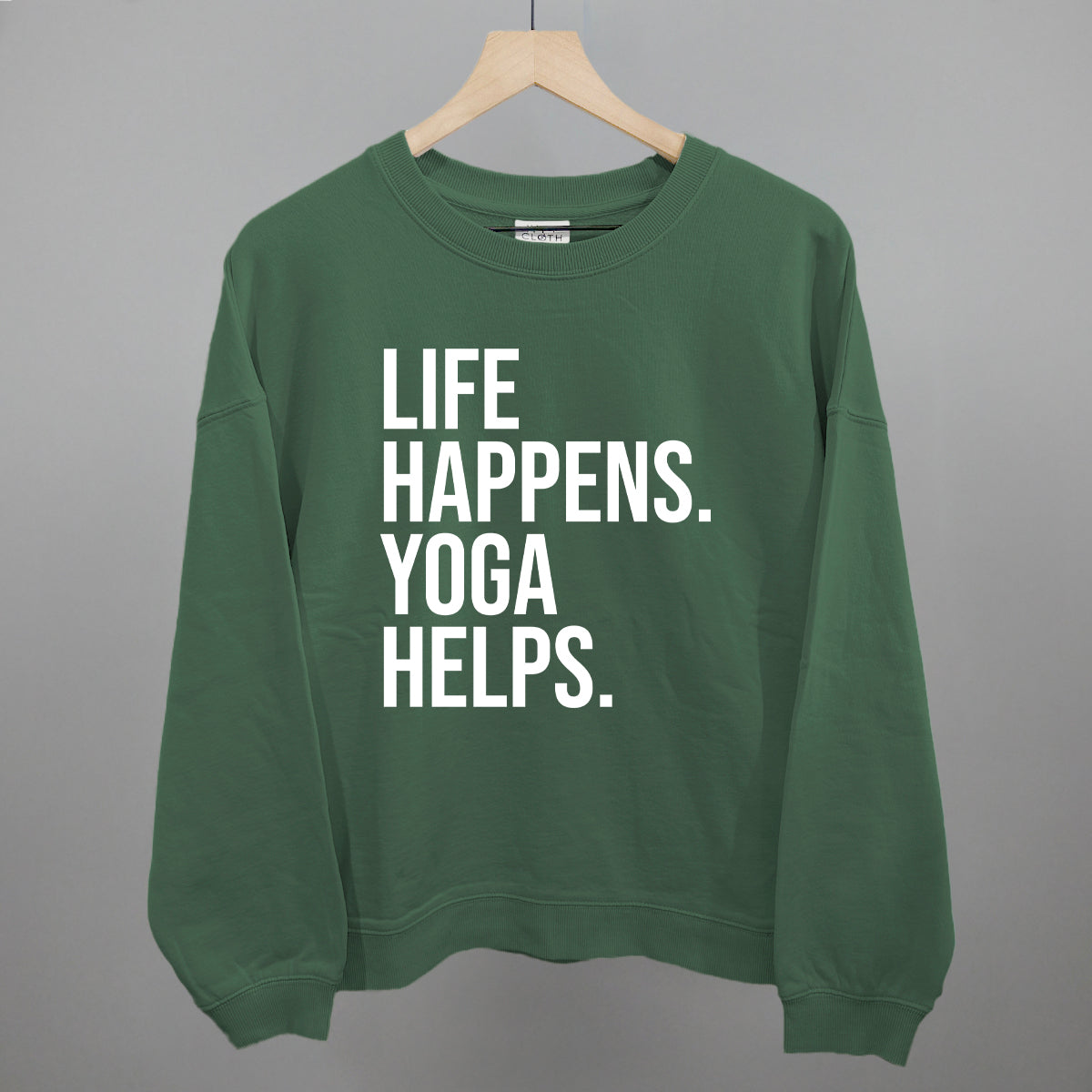 Green sweatshirt on a hanger with visible printed text, Life Happens. Yoga Helps.
