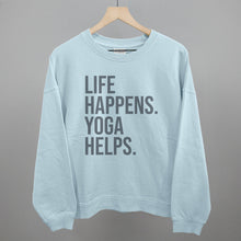 Light blue sweatshirt on a hanger with visible printed text, Life Happens. Yoga Helps.