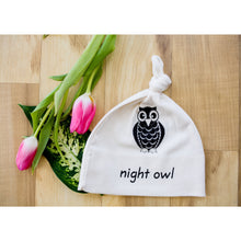 Natural cotton knotted baby hat with a black owl and Night Owl text beside pink tulips