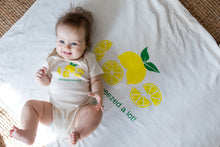 Baby lying on a natural cotton blanket with yellow lemon graphics and I Get Squeezed a Lot text