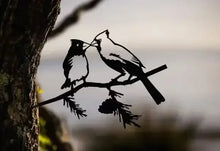 Two cardinal silhouette decorations on a branch beside a tree trunk.