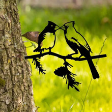 Two cardinal silhouette decorations on a branch attached to a tree trunk.