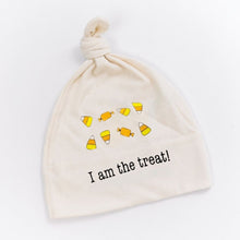 White knotted baby hat with candy corn graphics and “I am the treat!” text on a white background.