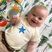 Smiling baby wearing a natural cotton short-sleeve romper with a blue A Star Is Born starfish design