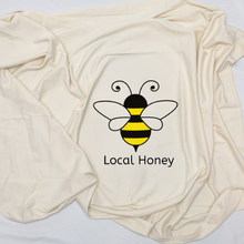 Natural cotton Local Honey baby blanket with a yellow and black bee folded on a white background