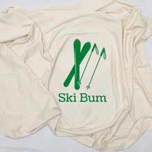Close view of a natural cotton baby blanket with green skis and Ski Bum text