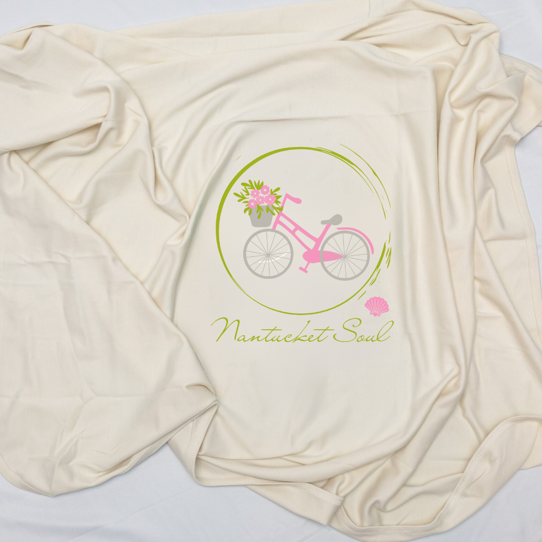 Close view of a natural cotton Nantucket Soul baby blanket with a pink bicycle and flowers