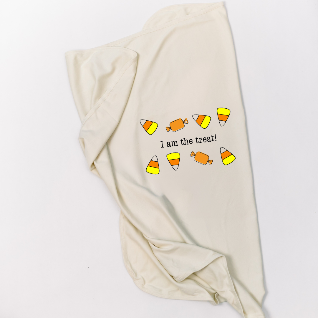 Natural cotton baby blanket with an I Am the Treat candy design folded on a white background