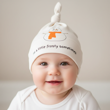 Baby wearing a white knotted hat with snowman graphic, orange scarf, and “I’m a little frosty sometimes!” text.