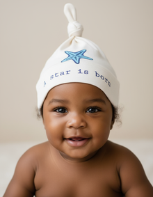 Baby wearing a natural cotton knotted hat with a blue starfish and A Star Is Born text