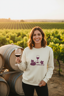 Woman wearing a natural cotton I Wine a Lot sweatshirt while holding a wine glass at a vineyard