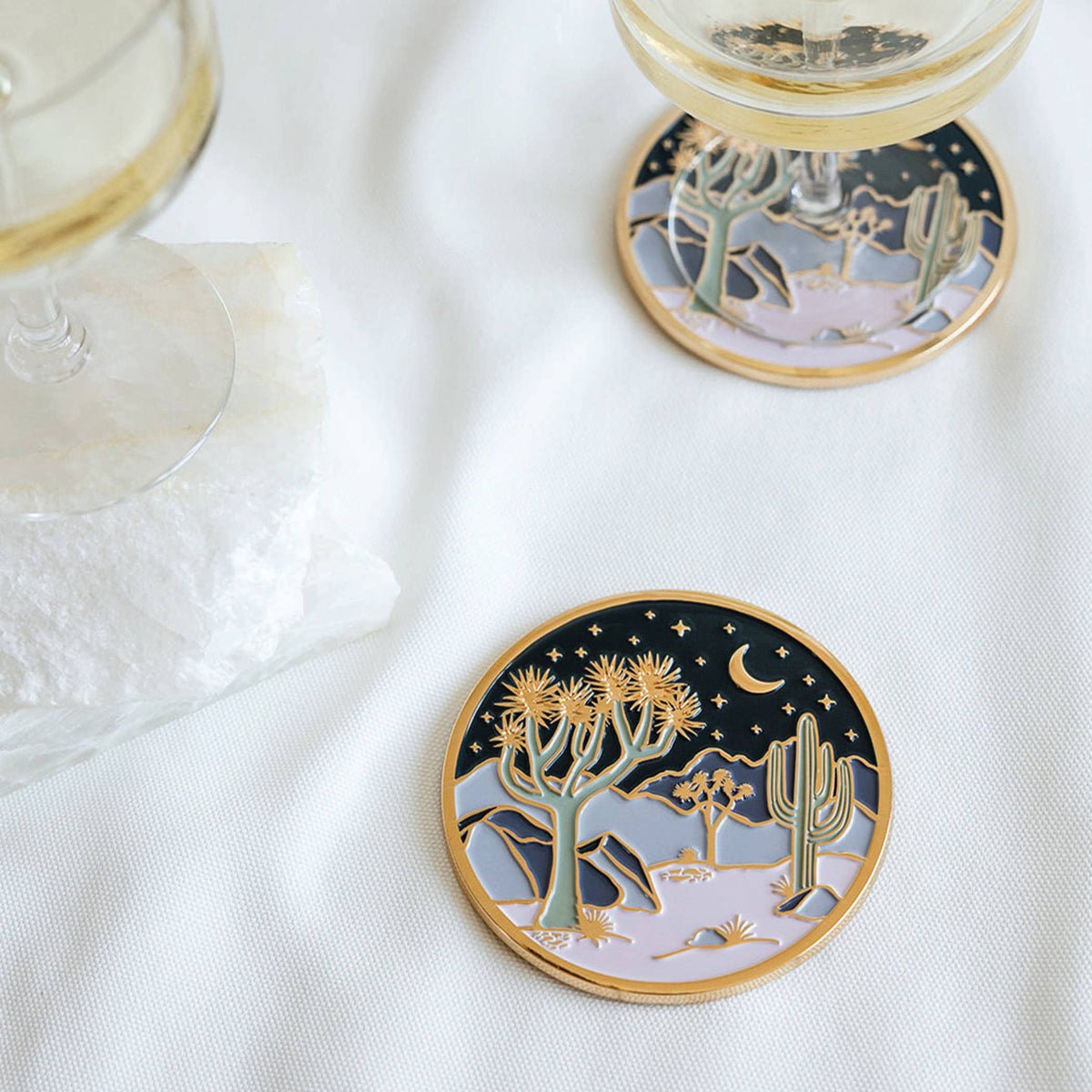 Two Moonlight Joshua Tree coasters styled beneath wine glasses on a white table
