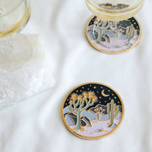 Two Moonlight Joshua Tree coasters styled beneath wine glasses on a white table