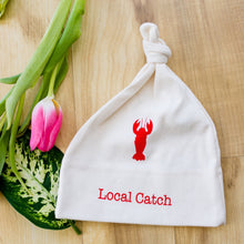 Natural cotton knotted baby hat with a red Local Catch lobster beside pink tulips