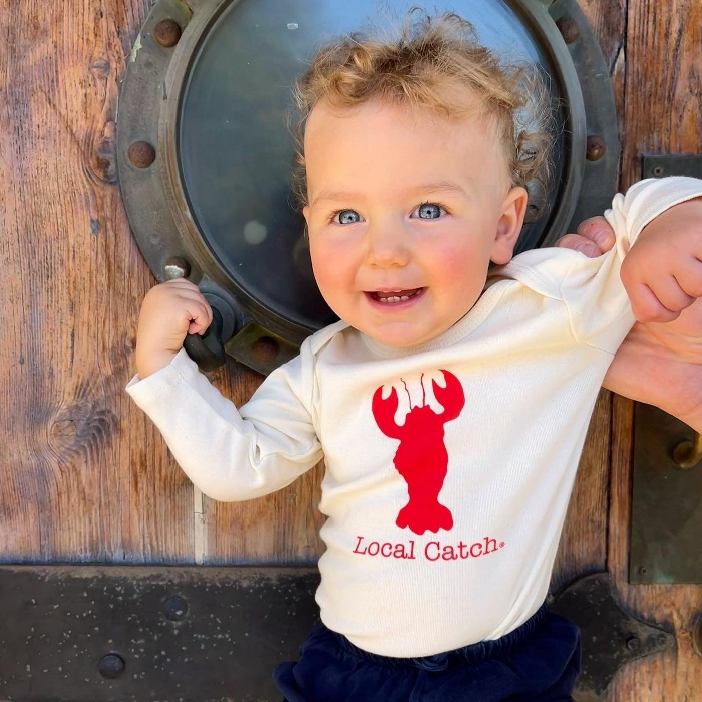 Toddler wearing a natural cotton long-sleeve romper with a red Local Catch lobster design