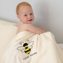Baby wrapped in a natural cotton Local Honey blanket with a yellow and black bee design