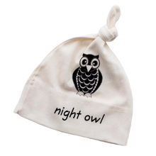 White knotted baby hat with black owl graphic and “night owl” text on a transparent background.