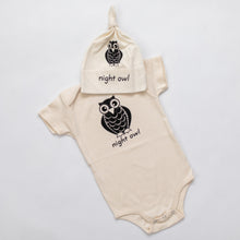 Natural cotton short-sleeve baby romper and hat with a black Night Owl design laid flat