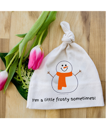 White knotted baby hat with snowman graphic, orange scarf, and “I’m a little frosty sometimes!” text beside pink tulips on a wood surface.