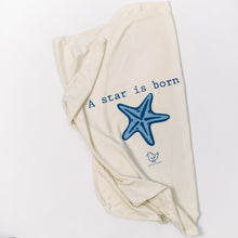 Natural cotton baby blanket with a blue starfish and A Star Is Born text folded on a white background